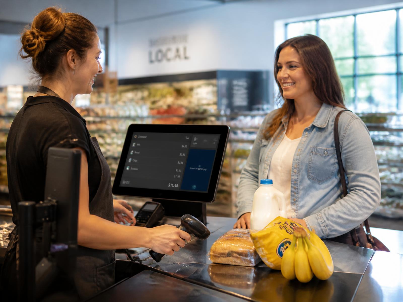 Cashier and customer at a retail checkout counter using a WECOMM POS terminal with barcode scanner and card payment terminal