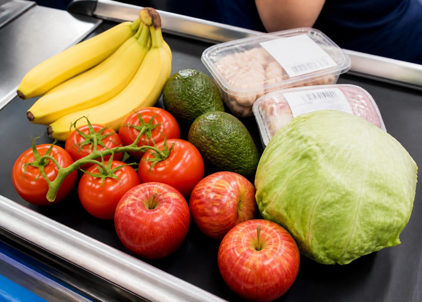 Grocery checkout belt with bananas, tomatoes, avocados, apples, lettuce and packaged barcoded items